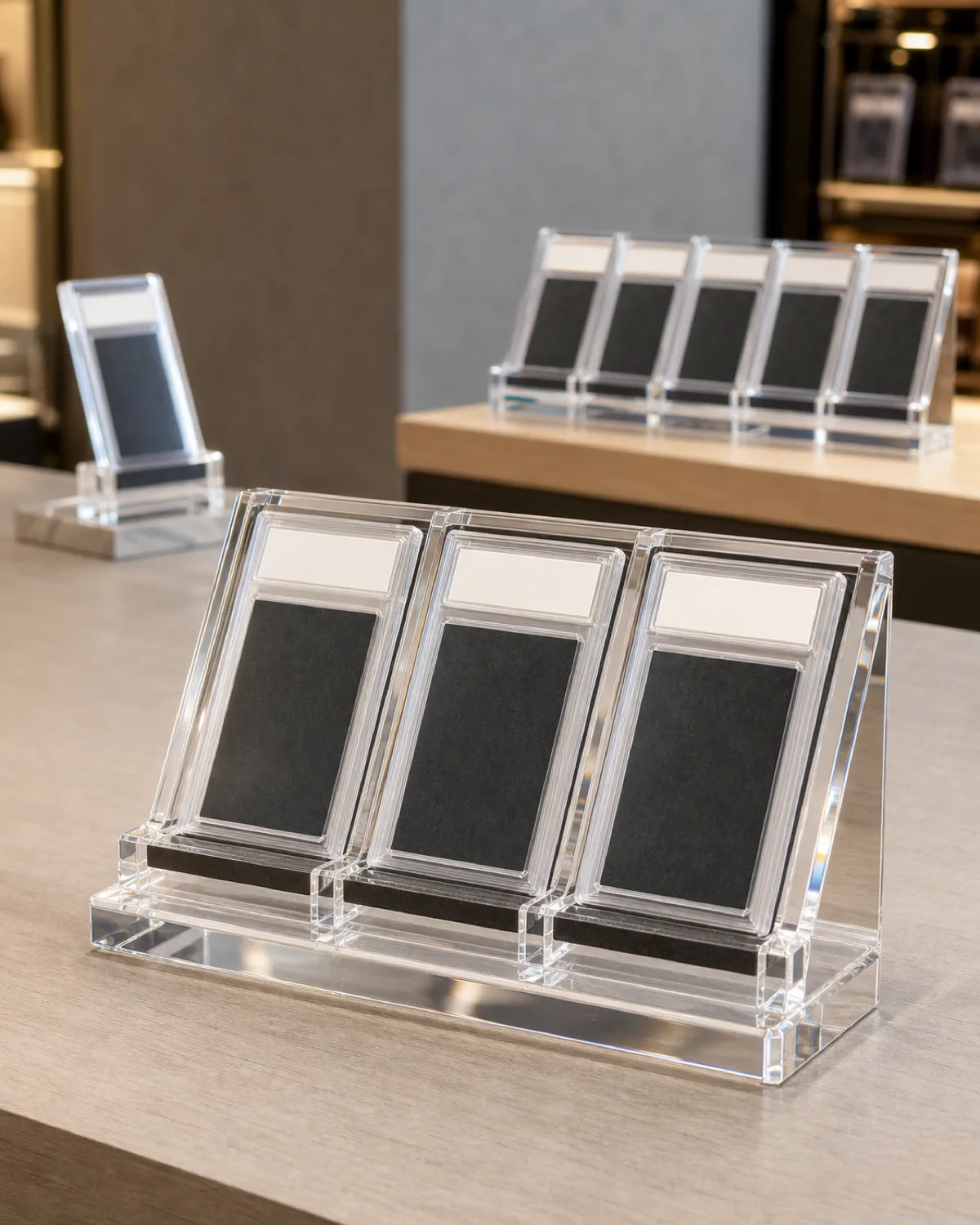 Clear acrylic Triple PSA slab display block holding three generic encapsulated graded card slabs in individual angled slots, beside a single-slab stand and a 6-slot slab block, on a retail counter