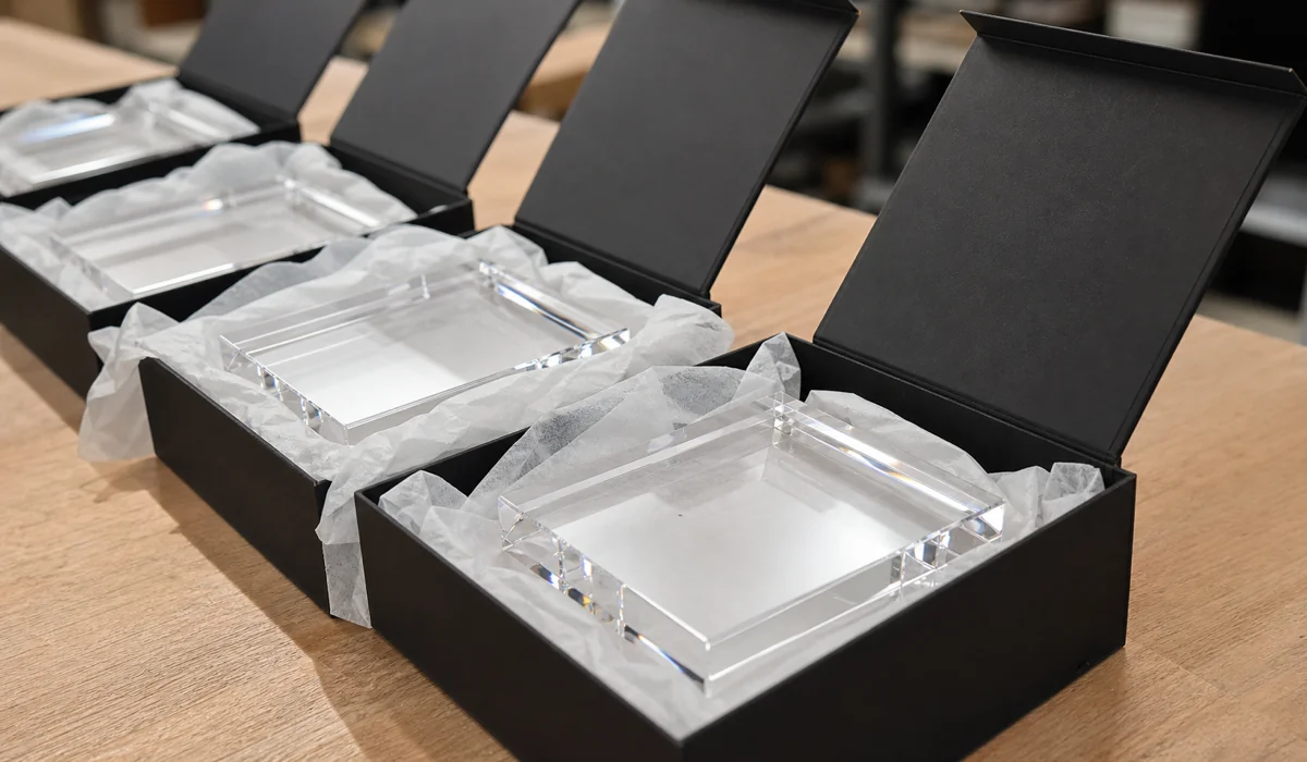 Row of blank clear acrylic photo blocks nested in tissue-lined gift boxes on a packing bench, ready for print lab fulfillment