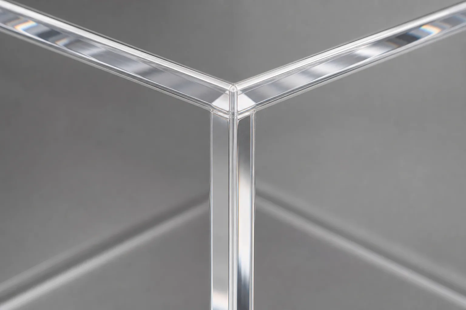 Close-up of a clear cast acrylic box corner with a clean solvent-bonded seam, light refracting along the polished PMMA edge against a neutral studio background
