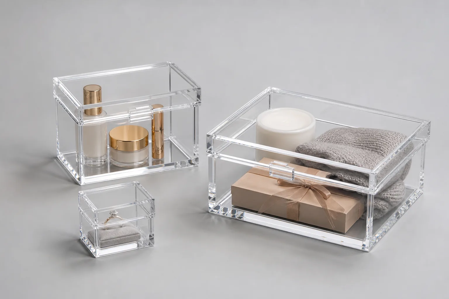 Three clear acrylic gift boxes in graduated sizes on a neutral surface, showing small ring-box, mid cosmetics-box, and large multi-item plexiglass gift box formats