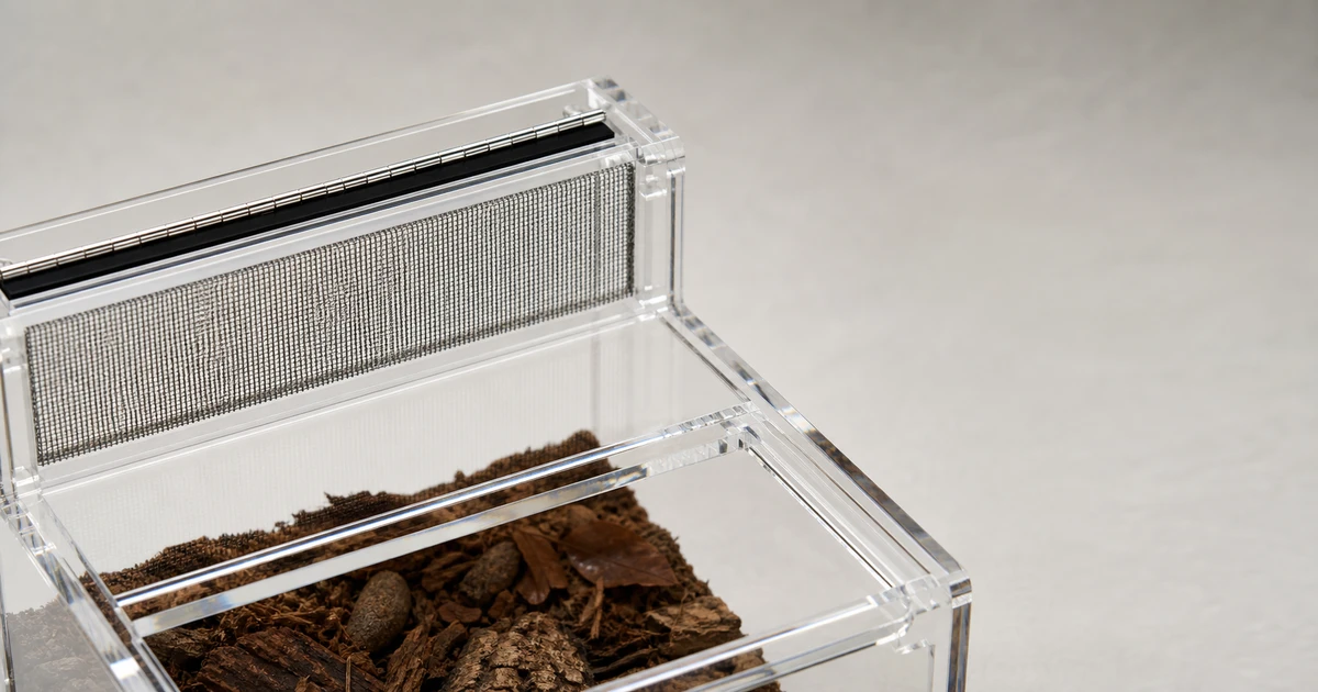 Top-down or rear-cutaway view of an acrylic reptile enclosure showing mesh ventilation panel and hinge gasket, soft directional light, no live animal