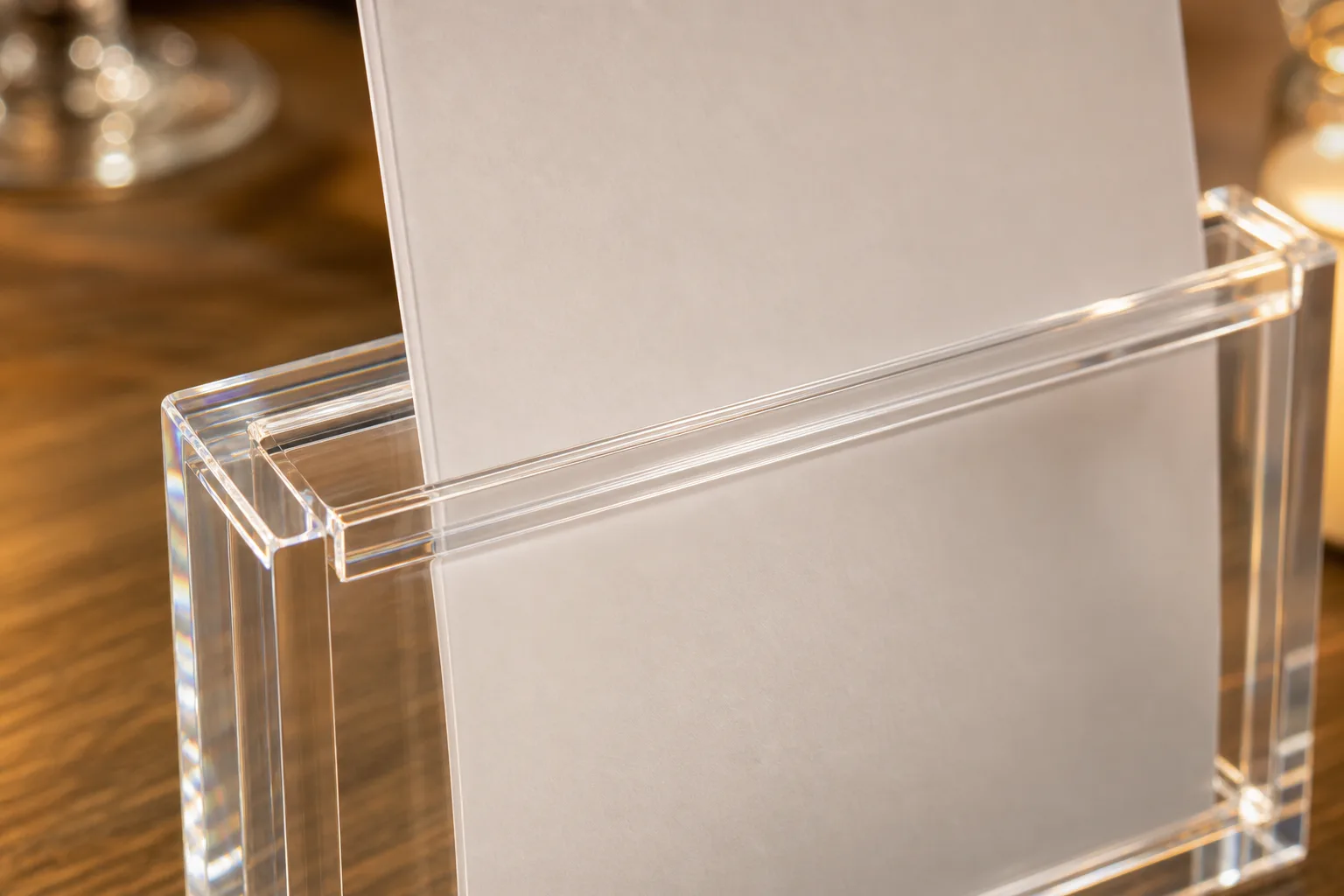 Close-up of a clear acrylic menu holder with a printed paper insert sliding into a CNC-routed top-load slot, polished sign holder edges catching the light