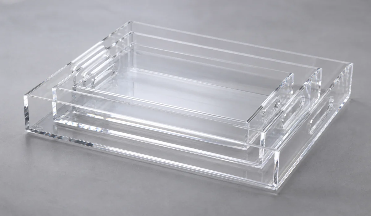 Three clear acrylic serving trays of different depths nested and stacked in a flat lay, showing how shallower PMMA trays nest tighter for carton packing
