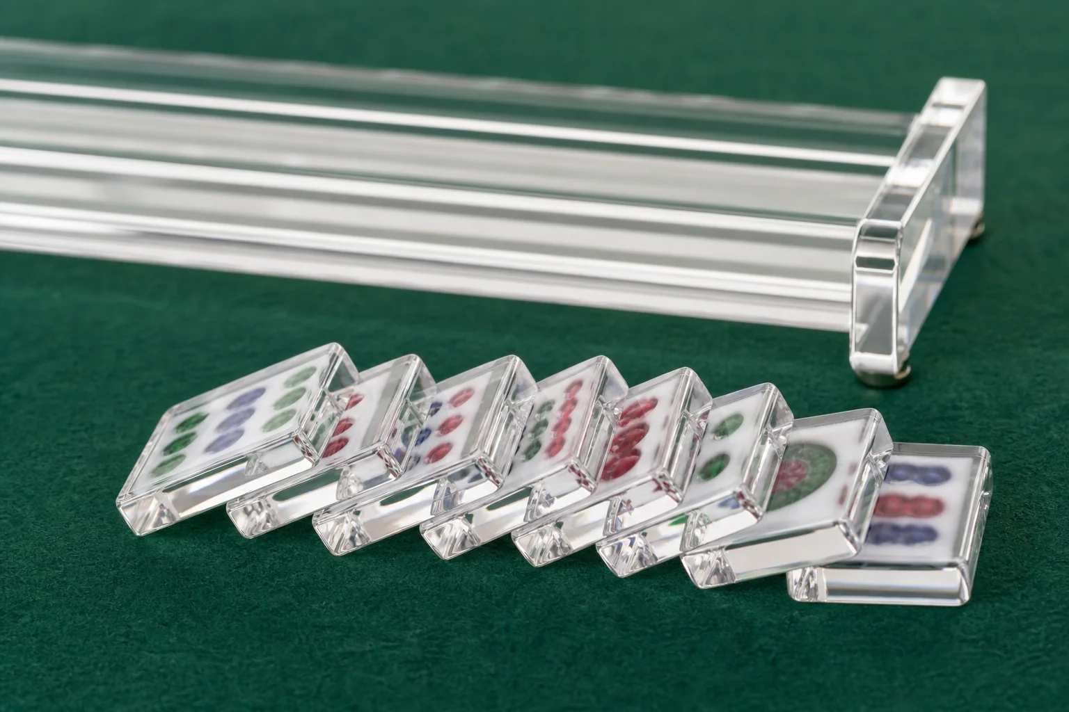 Acrylic mahjong tiles fanned on green felt beside a clear acrylic rack, translucent cast PMMA tile bodies, engraved faces softly out of focus