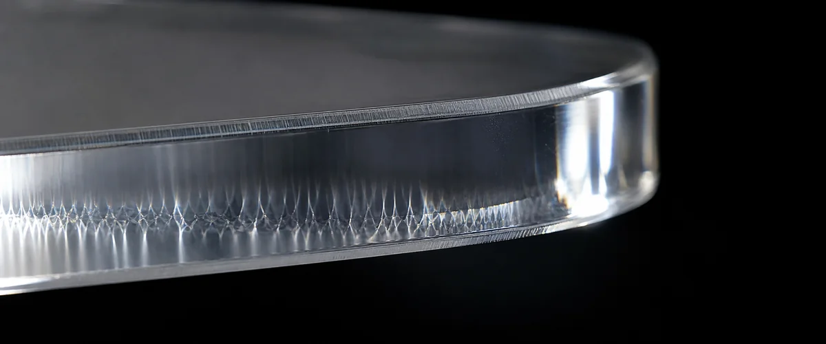 Extreme macro close-up of a 5mm cast acrylic edge showing real diamond-polished optics, internal light caustics, and the machining-to-polish transition layer that 3D renders cannot reproduce