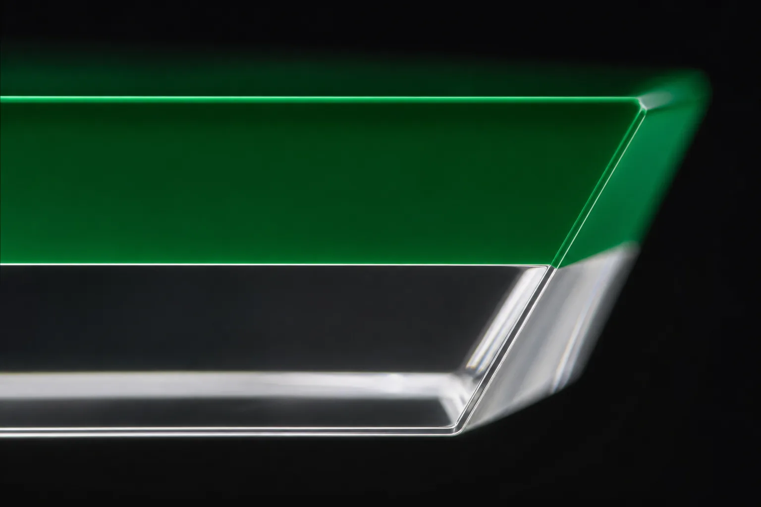 Macro view of a two-tone acrylic edge in raking light — a polished cast PMMA cross-section showing the clean horizontal bond line between a deep green base layer and clear top layer, free of bubbles and haze