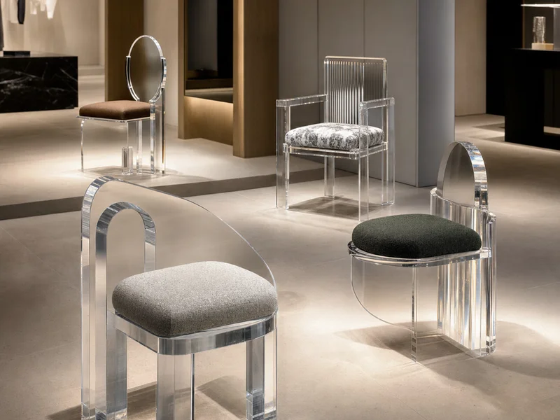 Luxury Retail Flagship — Sculptural Accent Chair. 4 accent chairs · custom one-off ergonomic design · molded clear cast PMMA · signature silhouette · bonded designer fabric seat · placed as visual centerpieces in flagship-store seating zones · custom mold tooling amortized into first run