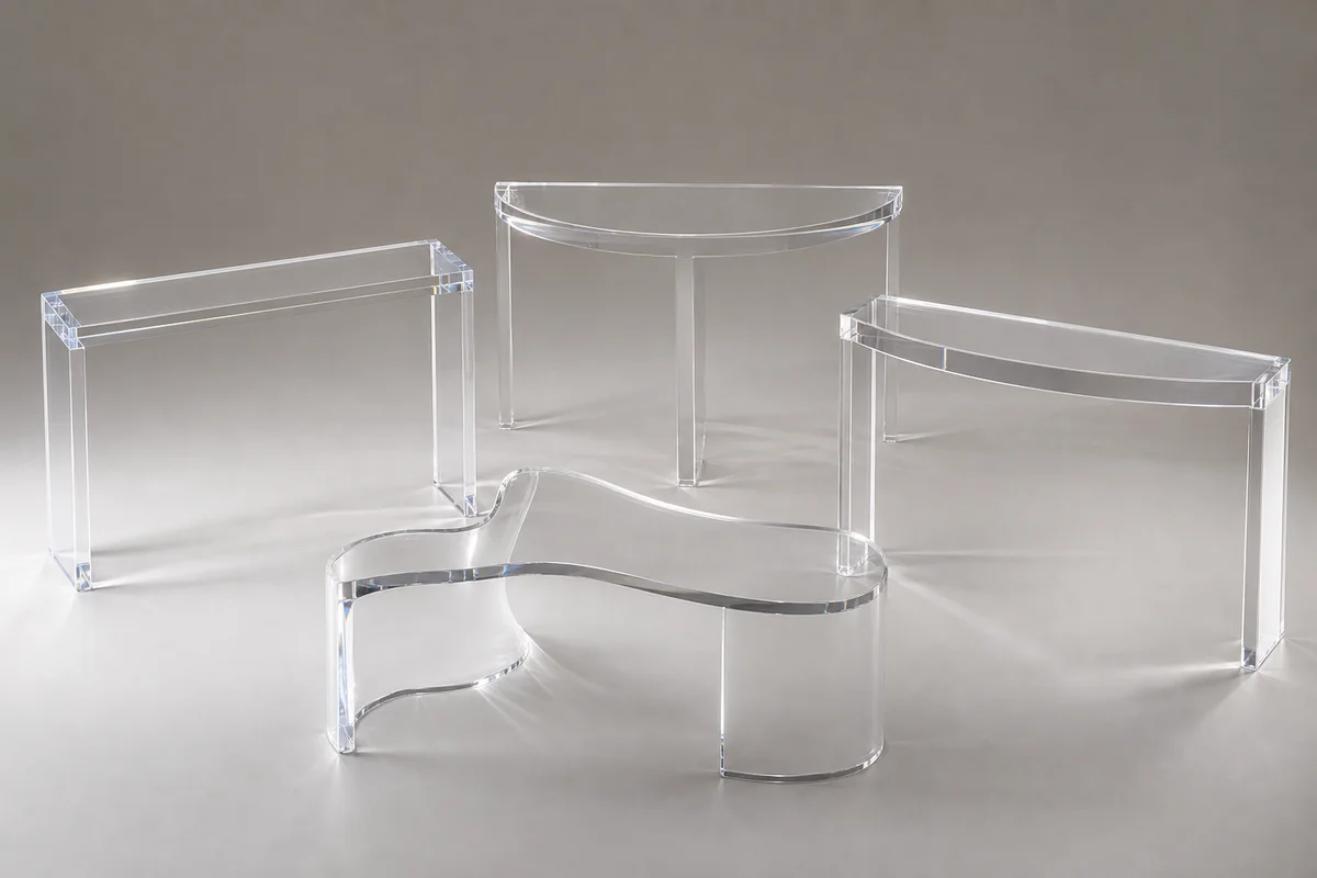Editorial group shot of clear cast acrylic console tables in different shapes — rectangular, demilune, asymmetric, curved-front — arranged together on a neutral surface