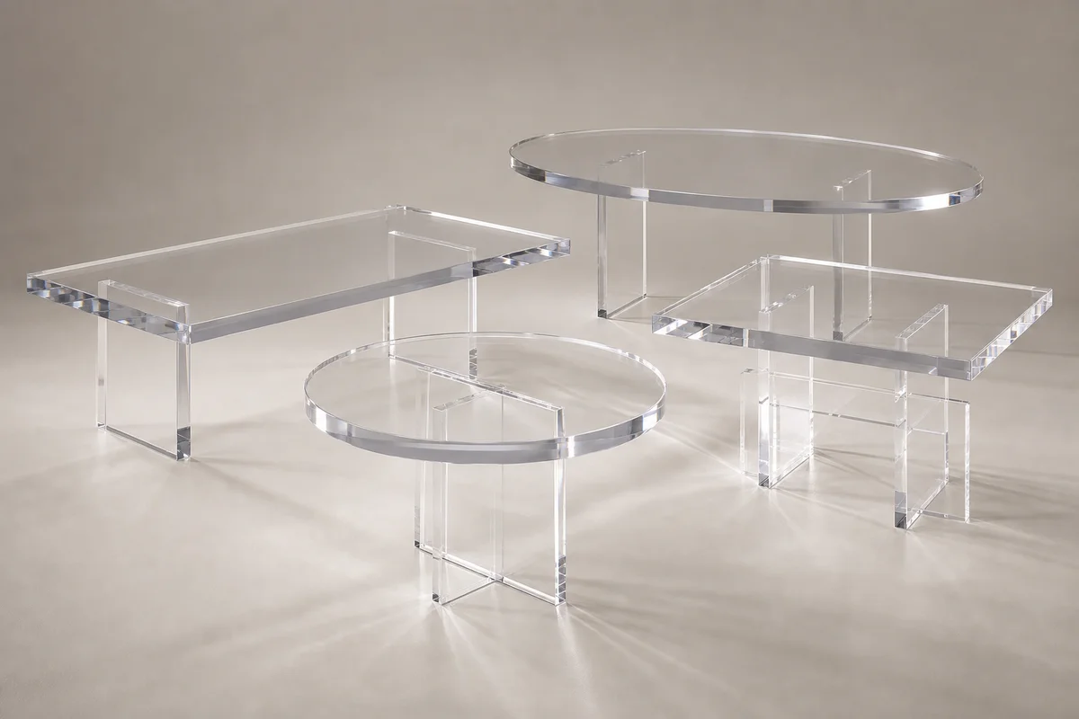 Editorial group shot of clear cast acrylic dining tables in different shapes — rectangular, oval, round, square — arranged together on a neutral surface with subtle warm lighting