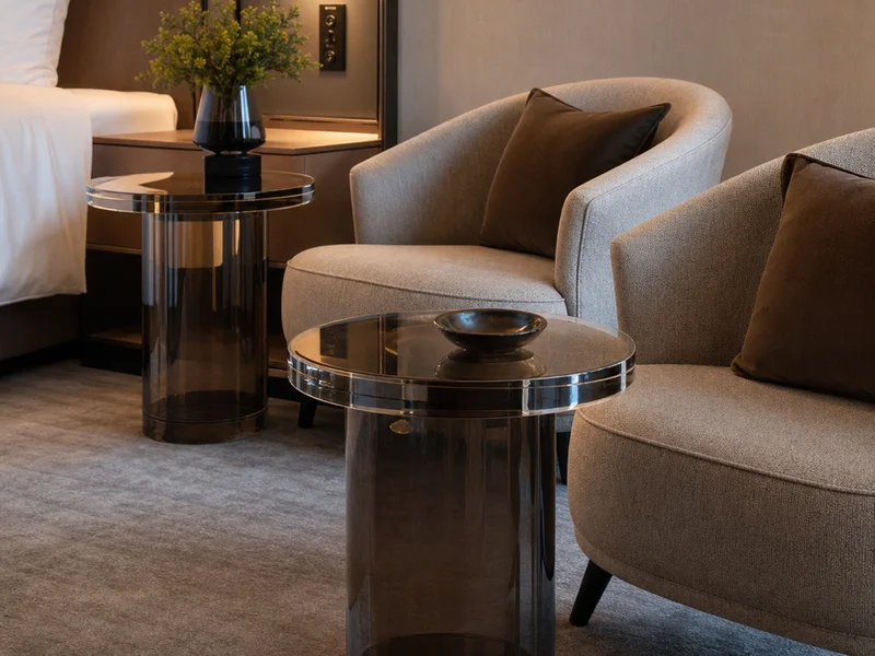 Boutique Hotel — 36 Guest-Room Round Pedestal Side Tables. 36 pieces · 22mm smoke-tinted cast acrylic · 50cm Ø top · single sculptural pedestal tapered 20% · bull-nose edge · brand-color smoke tint matched batch-to-batch across 12 properties
